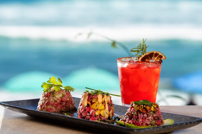 Three tartare towers beside a red cocktail with a dried orange slice